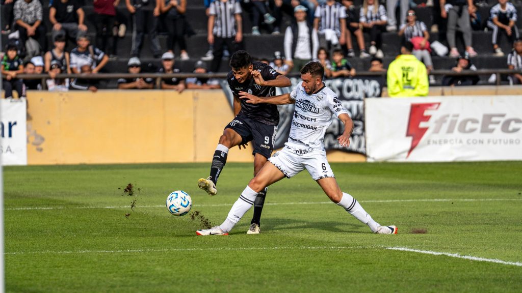 Intense soccer match moment with two players competing for the ball during day game.