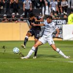 Intense soccer match moment with two players competing for the ball during day game.